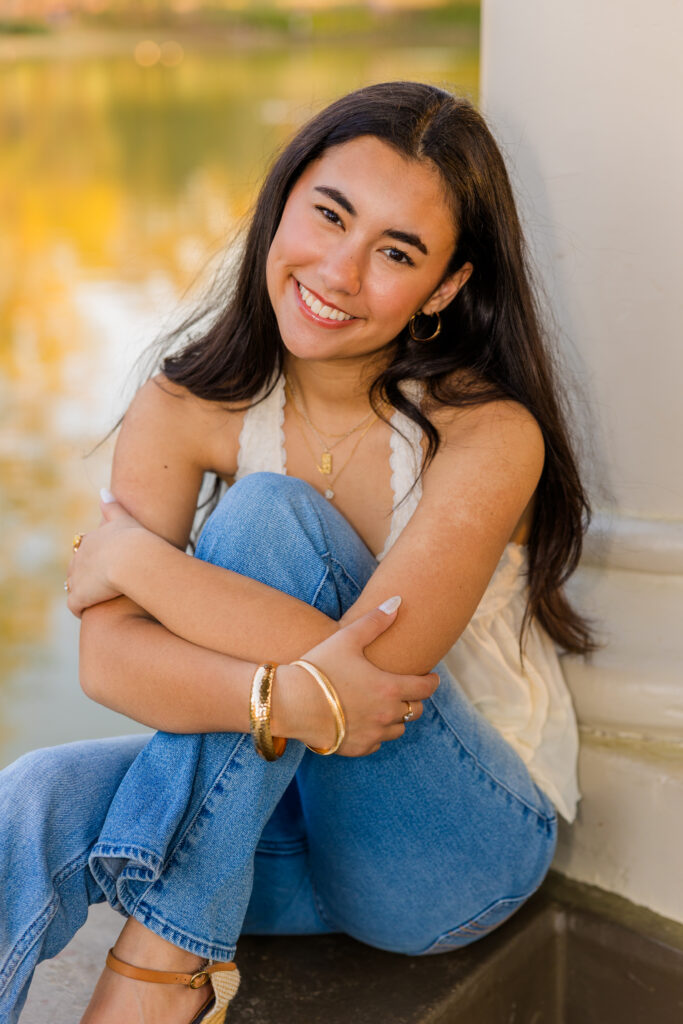 Senior sitting on wall smiling with pond in Piedmont Park