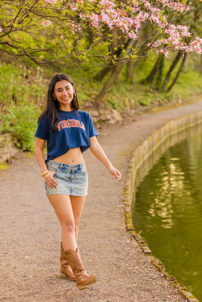 Senior in college gear walking by pond with flowers