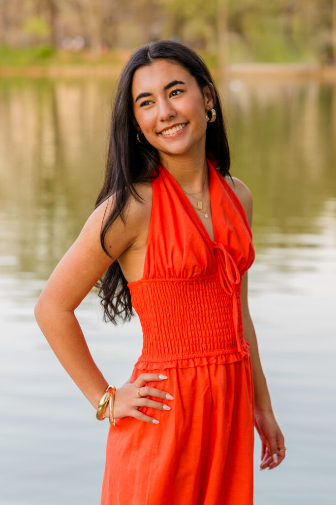 Senior in orange dress standing by pond in Atlanta park