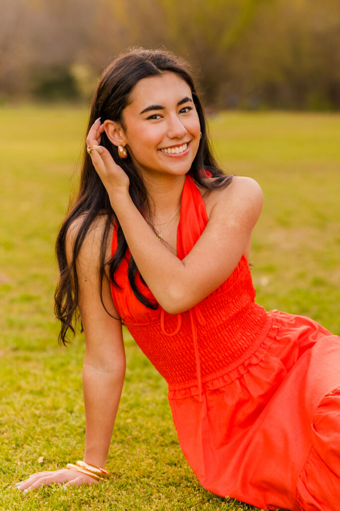 Senior sitting on grass in orange dress with hand in hair