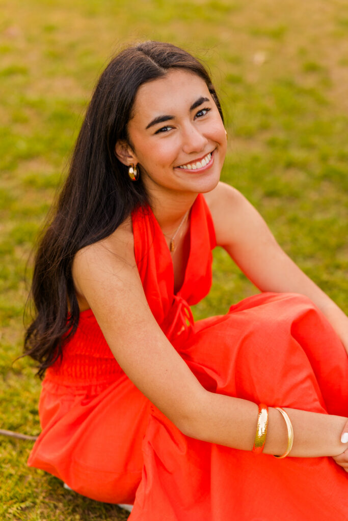 Overhead photo of senior in orange dress hugging knees