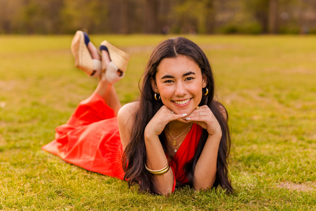Senior laying on stomach in orange dress resting head on hands