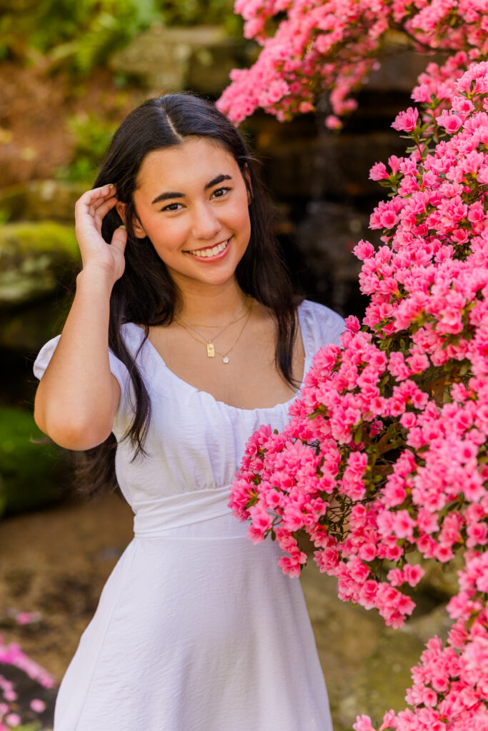 Atlanta senior in white dress posing with hand in hair next to blooming flowers