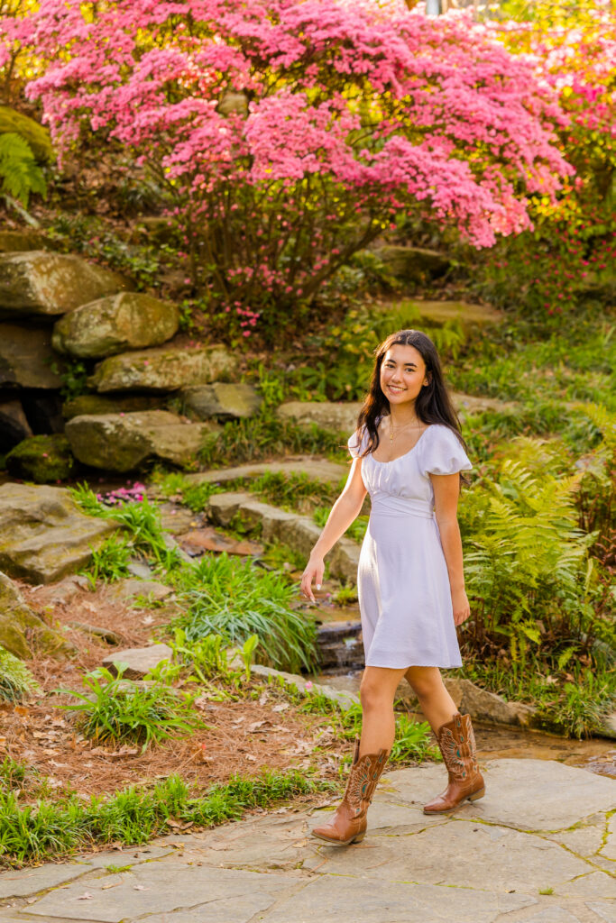 Senior walking in Atlanta park wearing white dress and cowboy boots with pink flowers