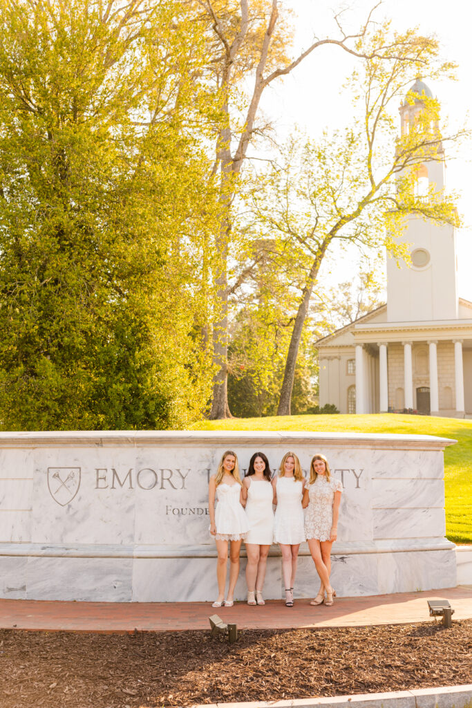 Four girls standing together in front of Emory University wall with sun through trees Atlanta
