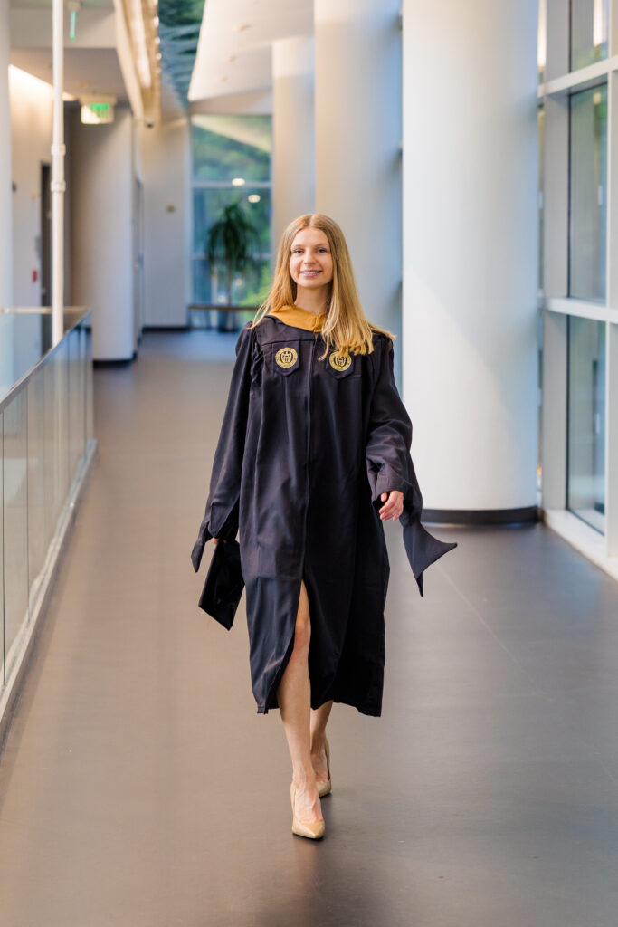 Gabriela walking through a hallway at Scheller College of Business holding her graduation cap
