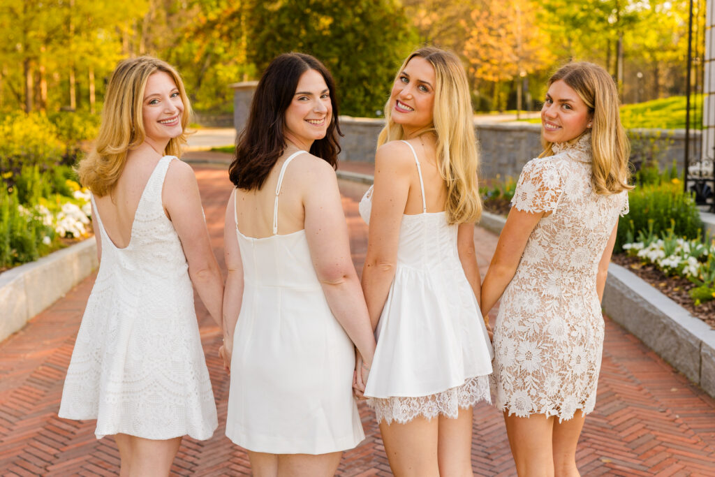 Four girls hands together looking at camera over shoulder during graduation session