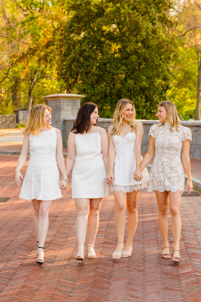 Four girls walking hand in hand looking at each other on Emory campus