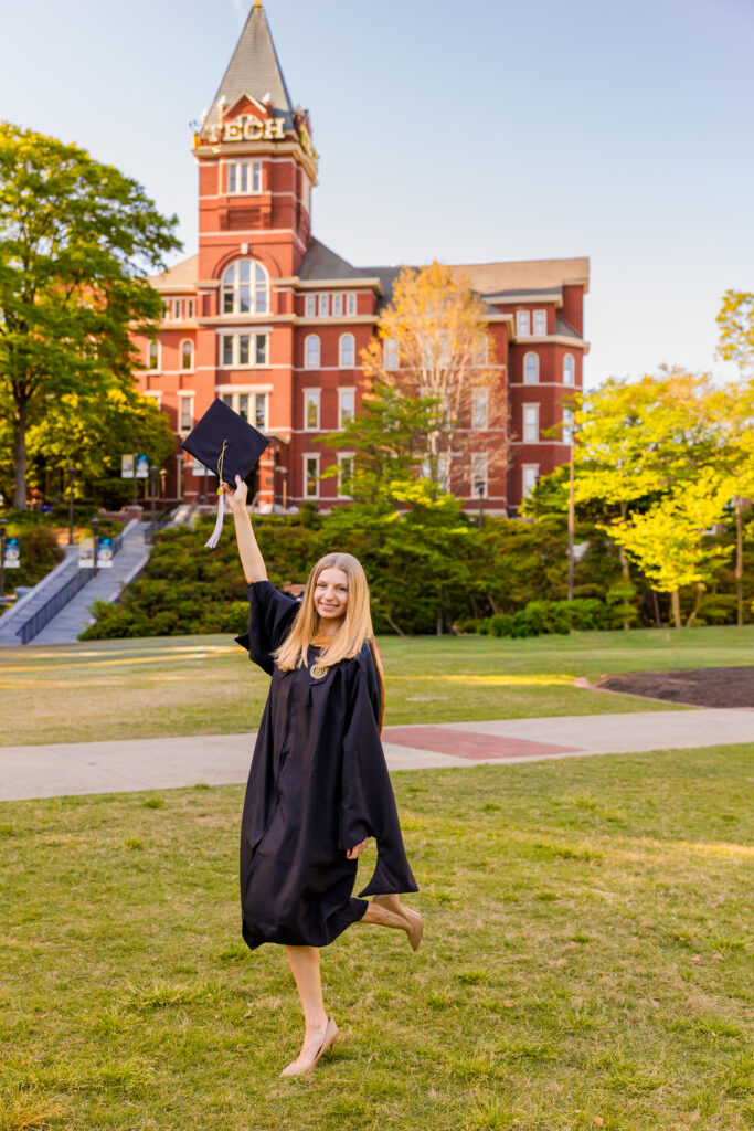 Gabriela posing with one leg up holding her graduation cap in front of GT Tower