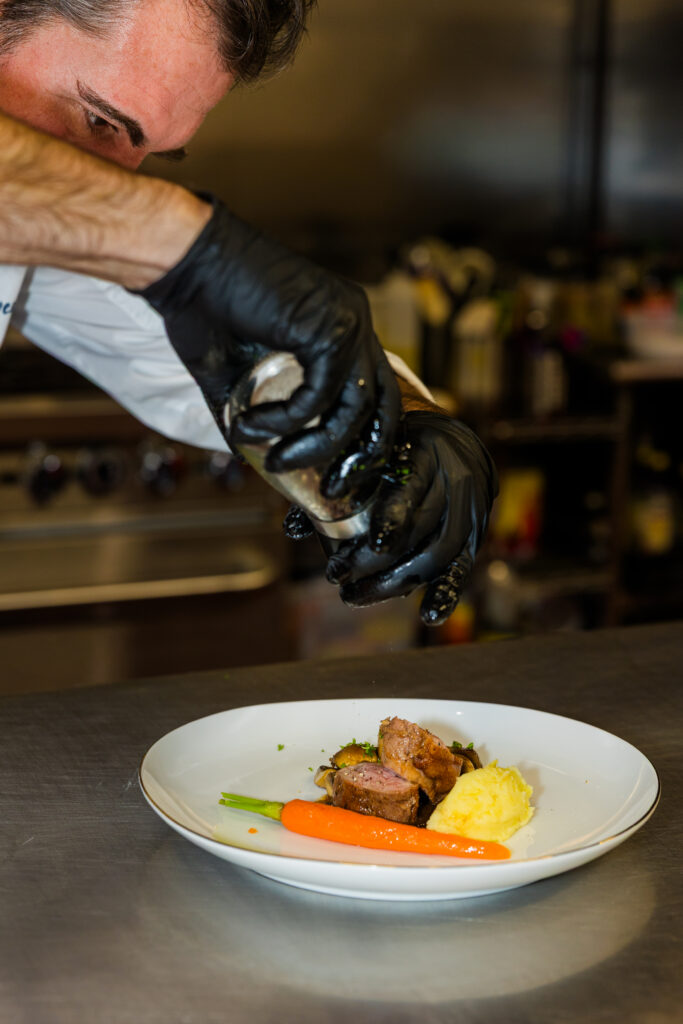 Chef adding final seasoning to plated meat dish