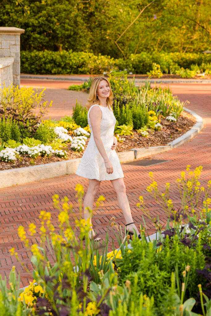 Cate walking across frame with flowers in foreground and background at Emory
