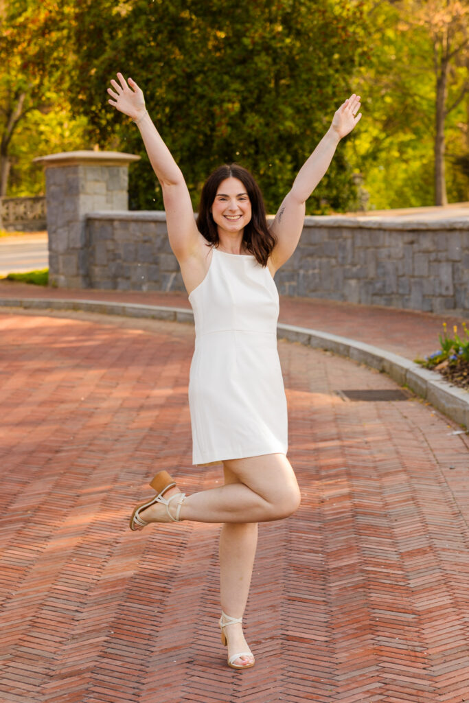 Roma laughing with one foot up and hands in the air during graduation photos