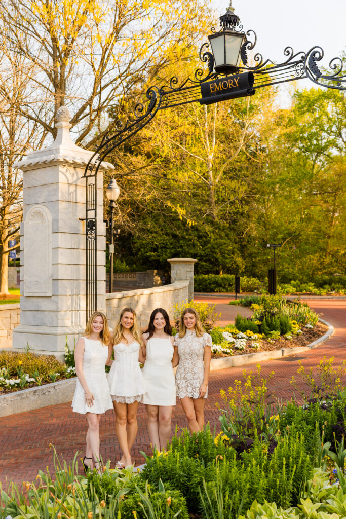Four girls hugging under Emory entrance arch with flowers during graduation session