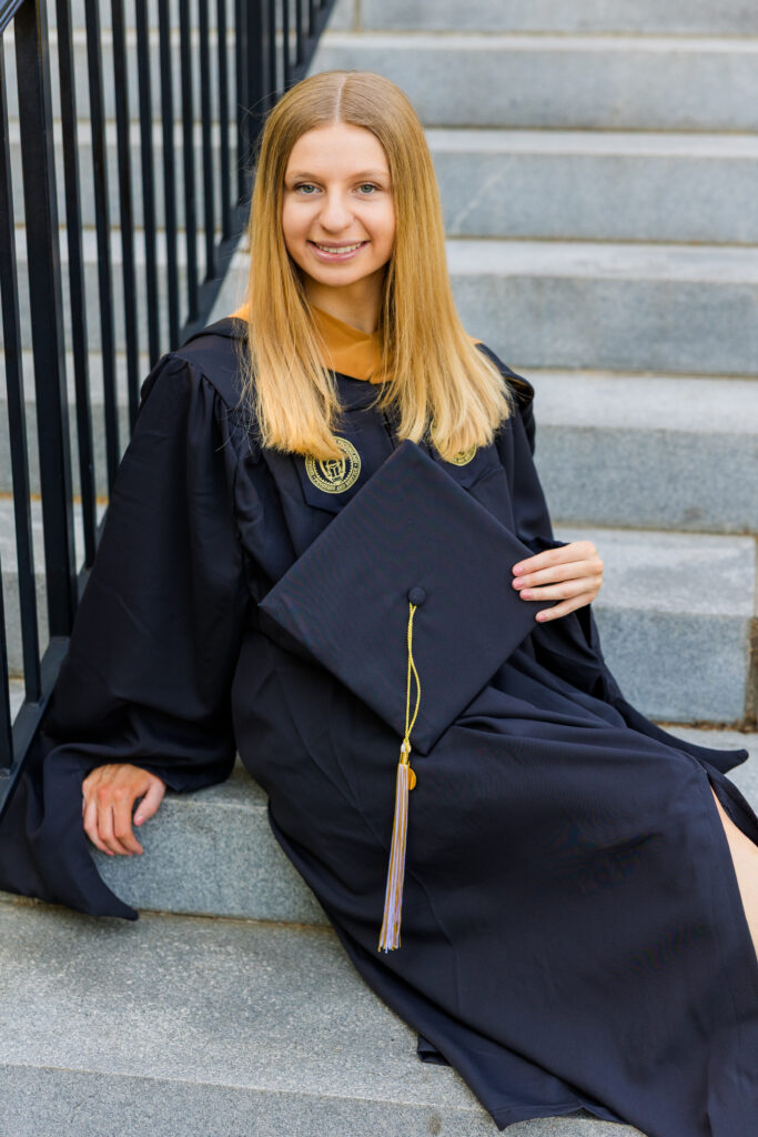 Gabriela sitting on the stairs at Georgia Tech in cap and gown