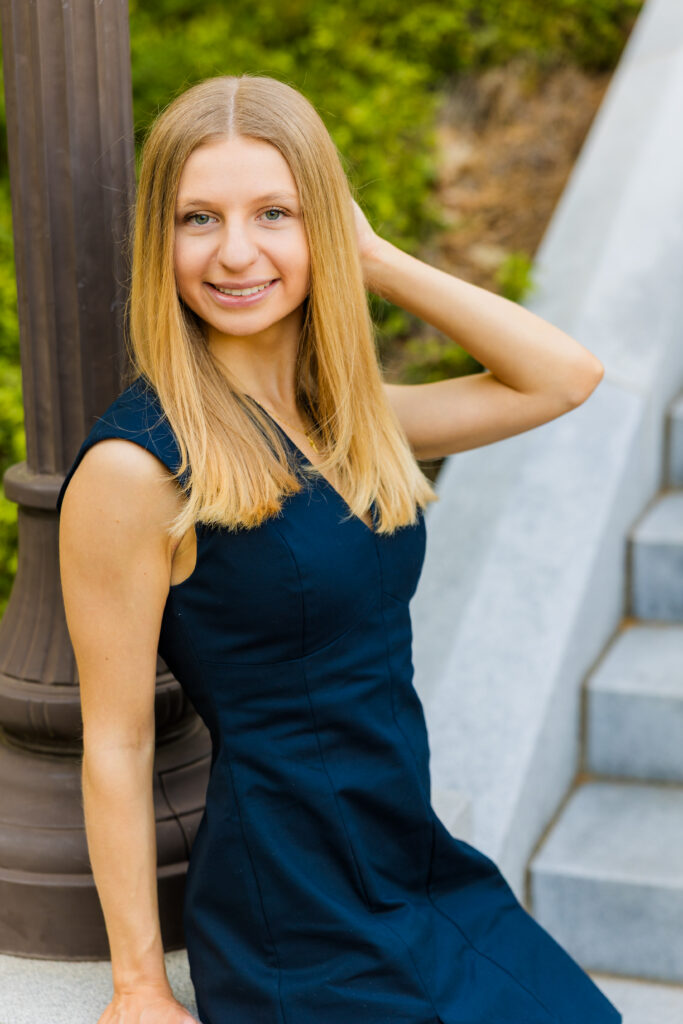 Gabriela sitting against a pillar in a dark blue dress during graduation photos