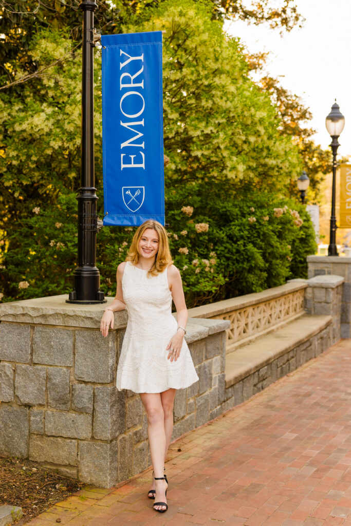 Cate leaning against wall with Emory banner behind her graduation photos