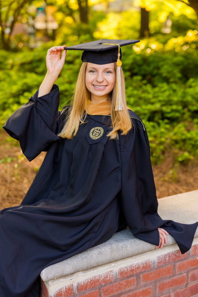 Gabriela sitting on a campus wall in cap and gown at Georgia Tech