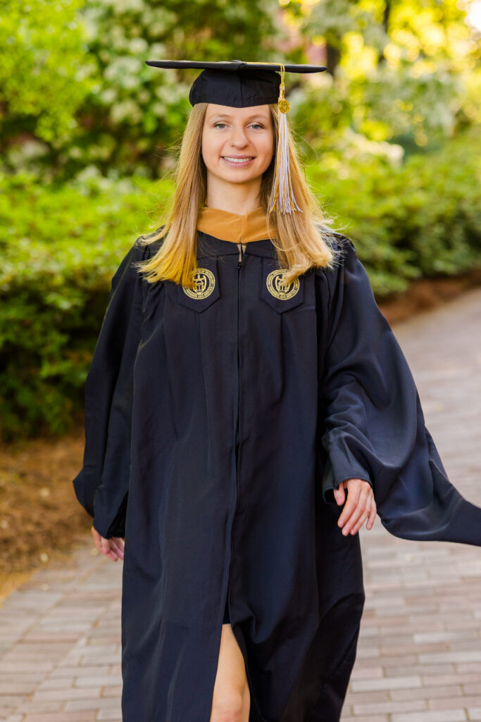 Gabriela walking on a path on Georgia Tech campus in cap and gown