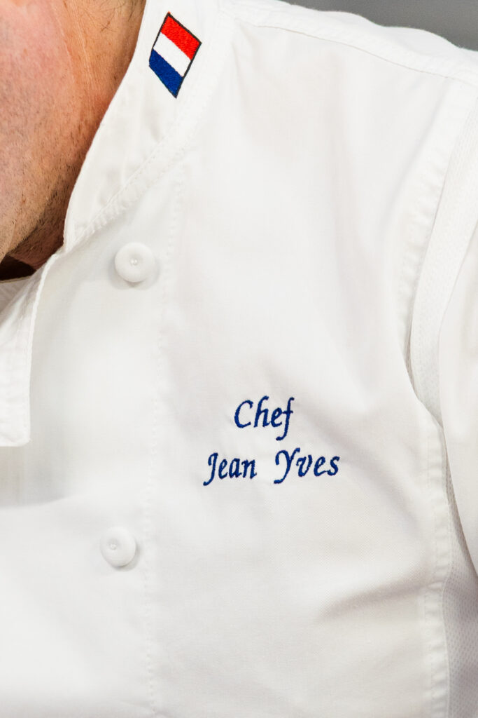 Close-up detail of chef jacket showing name and French flag in professional kitchen