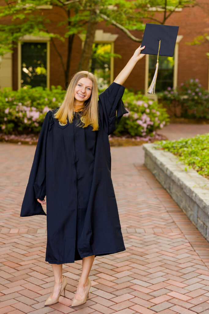 Gabriela standing in cap and gown holding her graduation cap in the air