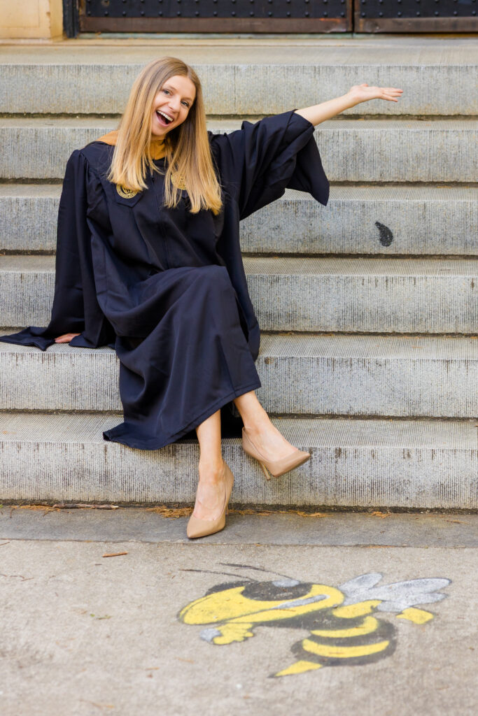 Gabriela sitting on stairs with the Georgia Tech bee drawing during graduation photos