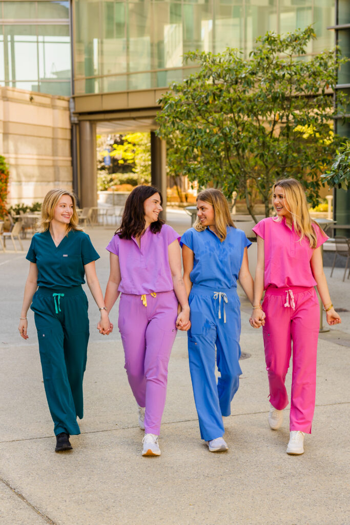 Wide shot of girls walking hand in hand in scrubs on campus