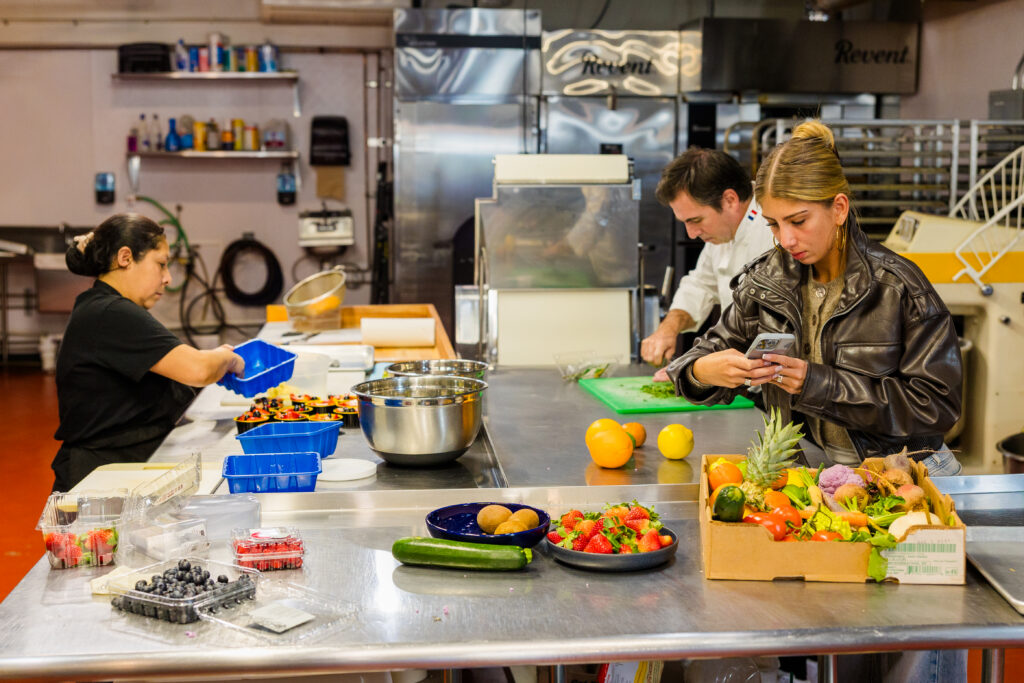 Wide kitchen scene with chef, team working and daughter taking photos