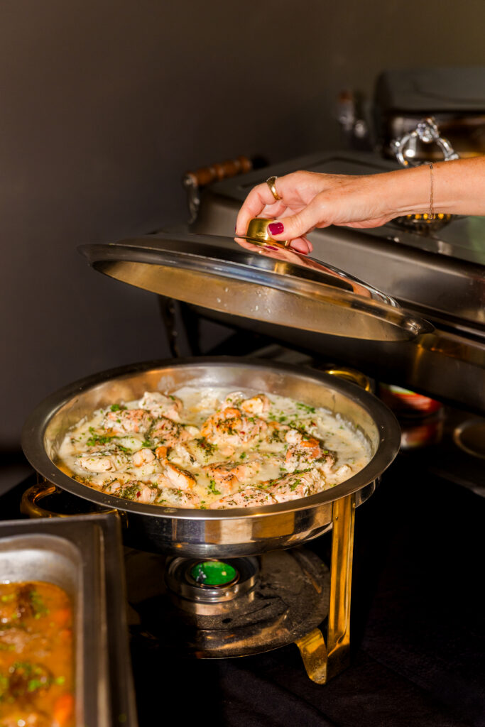 Hand opening catering pan lid revealing food inside