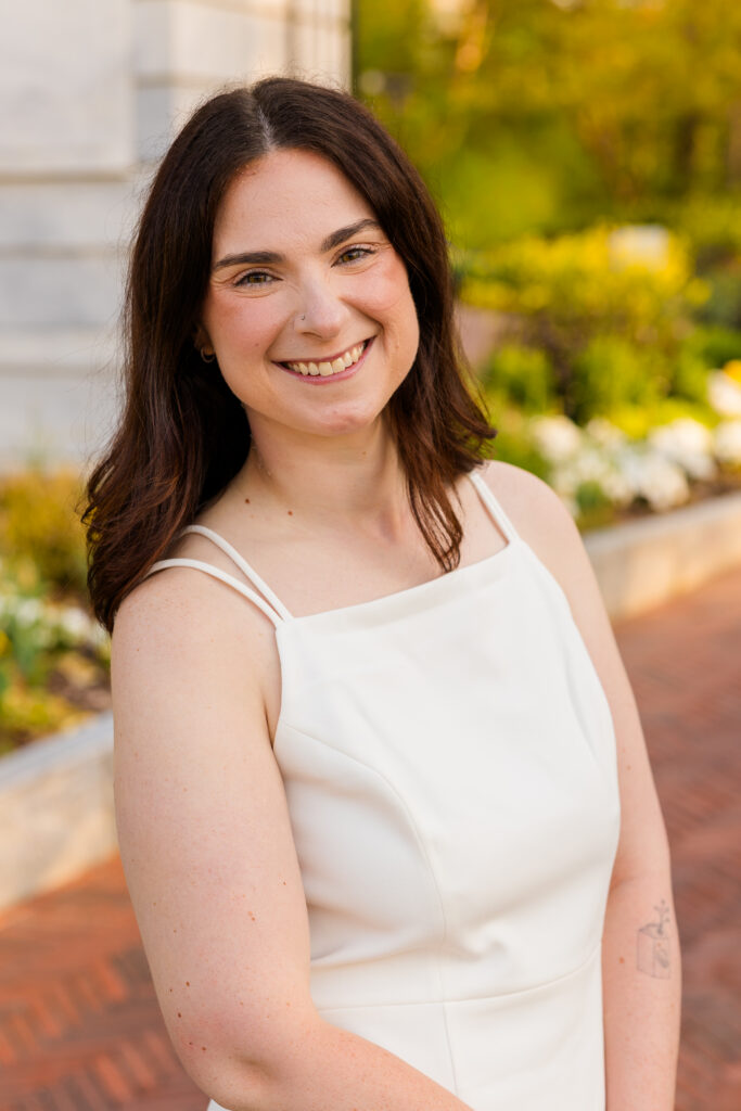 Close up of Roma in white dress with flowers in background at Emory graduation session Atlanta