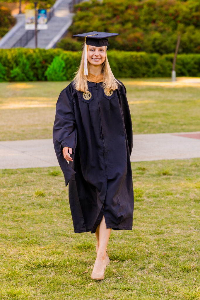 Gabriela walking toward the camera in cap and gown on Georgia Tech campus